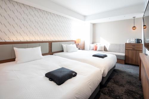 a bedroom with two beds with white sheets and a couch at HOTEL FORZA HAKATAEKI CHIKUSHIGUCHI Ⅱ in Fukuoka