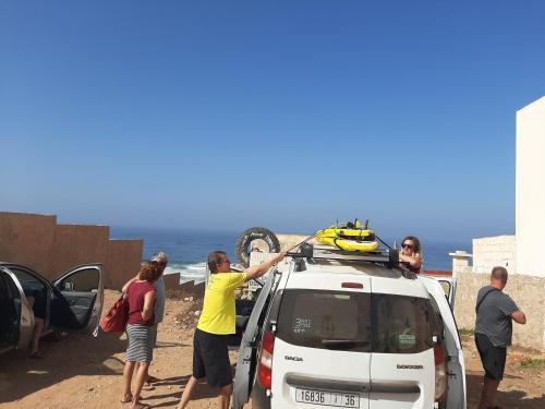 a group of people standing around a car on the beach at Auberge Maison Diyani in Sidi Ifni