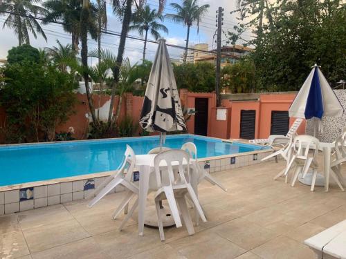um grupo de cadeiras e guarda-sóis ao lado de uma piscina em Hotel Canto da Enseada no Guarujá