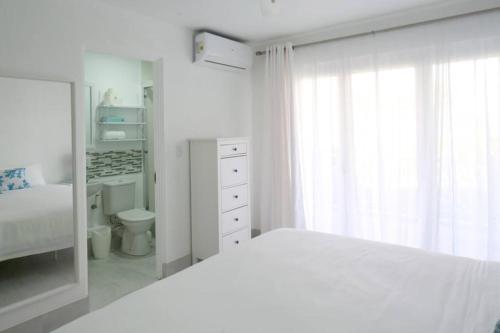 a white bedroom with a white bed and a bathroom at Sea Glass Villa - Spacious 1 Bed, 2 Bath on West Coast in Saint James