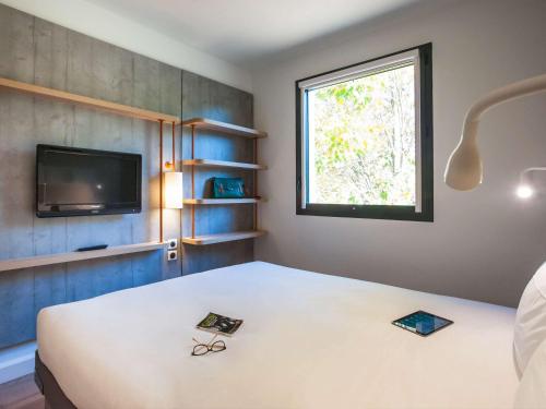 エソーム・シュル・マルヌにあるibis budget Château-Thierryのベッド、テレビ、窓が備わる客室です。