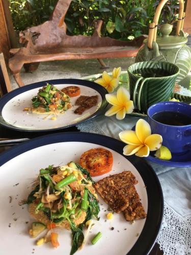 zwei Teller Essen auf einem Tisch mit Blumen in der Unterkunft Bali Firefly BnB in Ubud