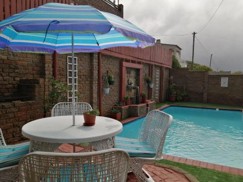 a table and chairs with an umbrella next to a pool at Amzee Bokmakierie Guest House in Dana Bay