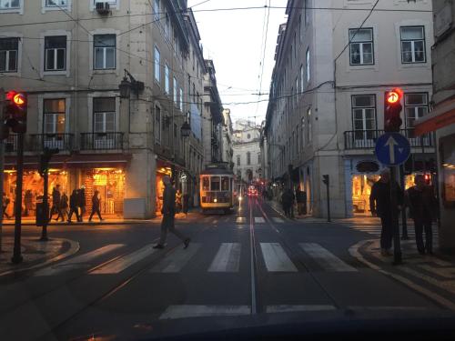 a city street with a tram and people crossing the street at Draft Hostel & Rooms in Lisbon