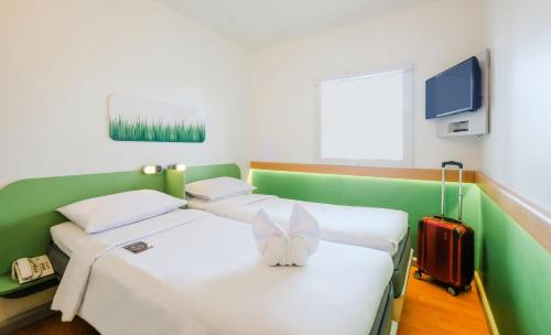 two twin beds in a room with a red suitcase at Cordia Hotel Makassar Airport in Makassar