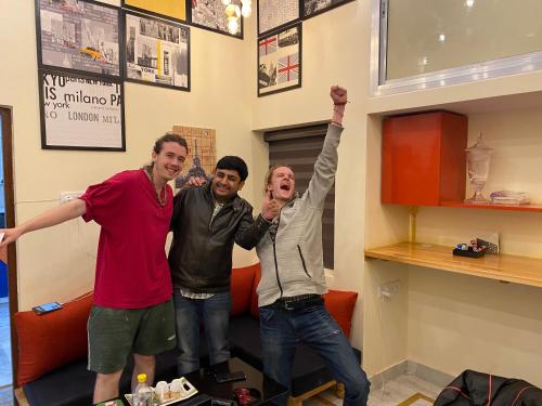 three men standing in a room with their arms in the air at Backpackers Den in Lucknow