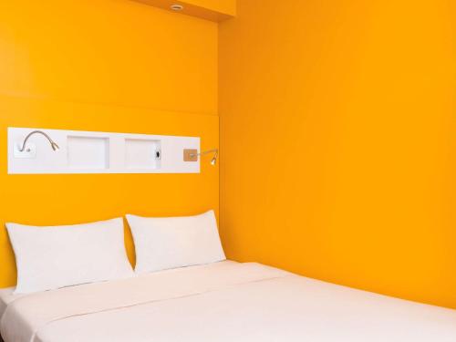 a bed in a room with an orange wall at ibis budget Paris Clichy Mairie in Clichy