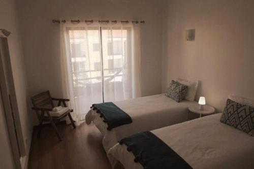 a bedroom with two beds and a window with a chair at Pedra do Ouro Yoga Retreat apartment in Pataias