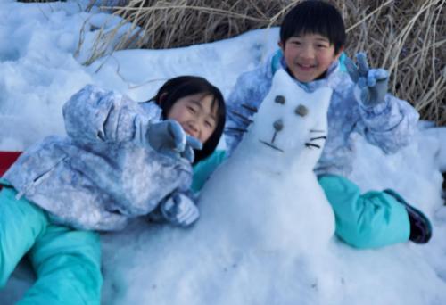 two children playing in the snow with a snowman at プチホテル葡萄屋 in Hakuba