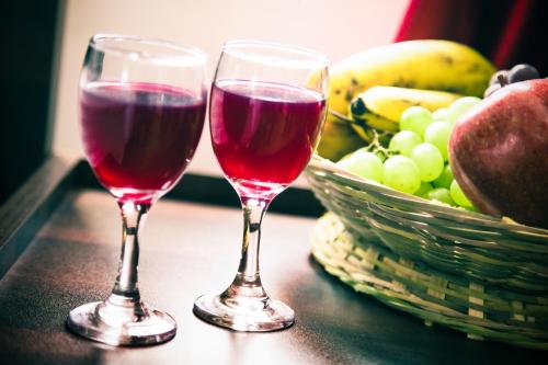two glasses of red wine next to a basket of fruit at Wayanad Three Roots Holiday Home Resort in Sultan Bathery