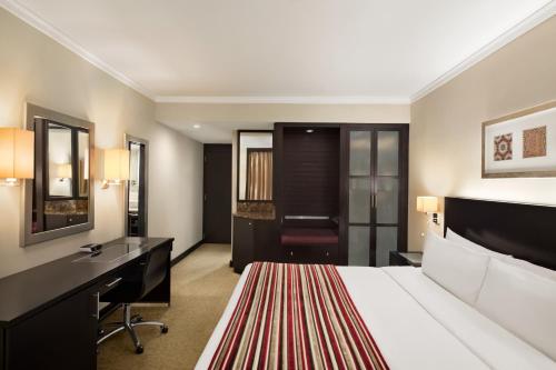 a hotel room with a bed, chair, desk and a television at Ramada Plaza by Wyndham Dubai Deira in Dubai