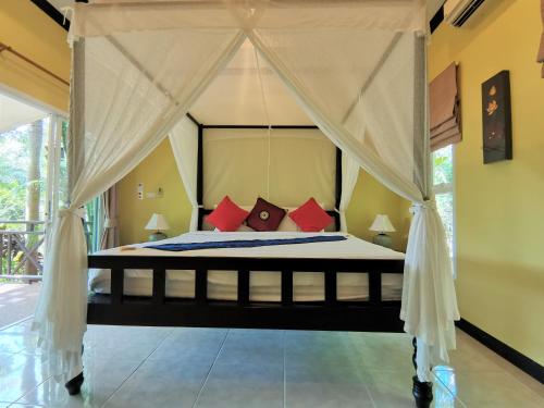 Thai Modern Resort & Spa في تشالونج: غرفة نوم مع سرير المظلة مع الوسائد الحمراء