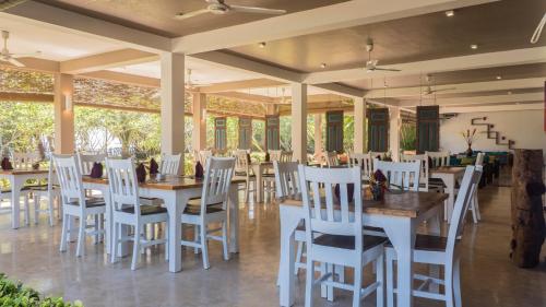 un comedor con sillas blancas, mesas y ventanas en Soul Wellness and Ayurveda Resort, en Dikwella