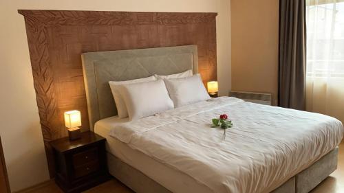 a bedroom with a white bed with a flower on it at Dolomiti Apartments in Bansko