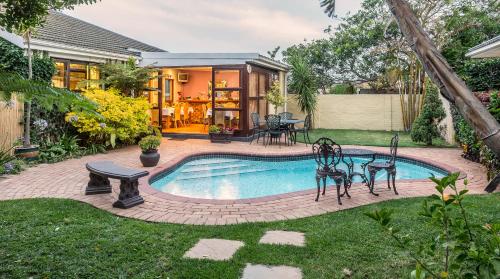 a backyard pool with a table and chairs next to a house at Algoa Guest House Summerstrand in Port Elizabeth