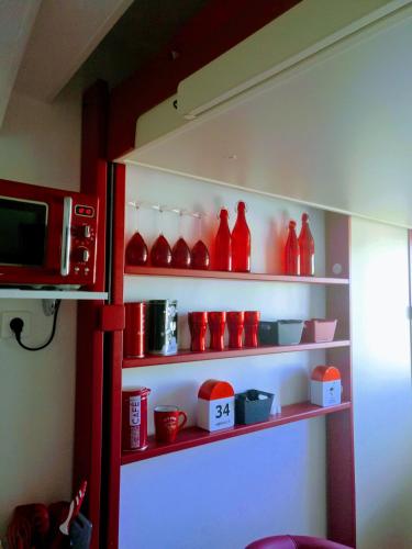 une étagère remplie de vases en verre rouge et d'un four micro-ondes dans l'établissement Le Bâbord - petit studio ambiance bateau à 30 m de la mer, à Palavas-les-Flots