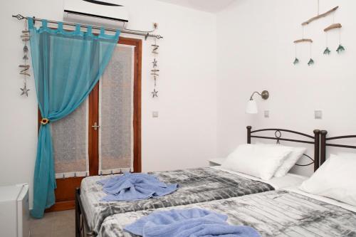 a bedroom with two beds and a window with blue curtains at Bella Vita Style rooms & apartments in Pitsidia