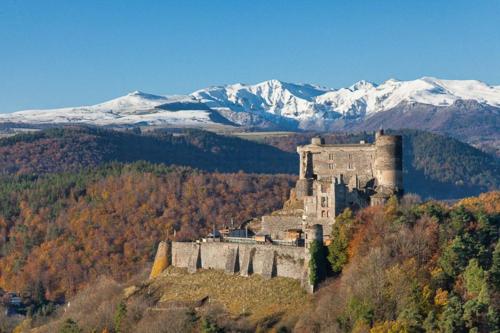 a castle on a hill with snowy mountains in the background at L OUSTALOU MAISON D HOTES DE CHARME EN AUVERGNE PISCINE PRIVEE CHAUFFéE in Saint-Nectaire