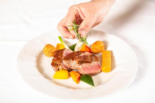 a person holding a piece of meat with vegetables on a plate at Kinder- & Gletscherhotel Hintertuxerhof in Tux