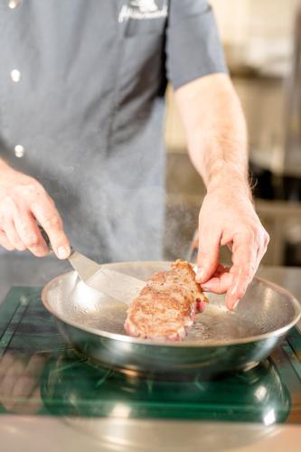 a man is cooking a piece of meat in a pan at Kinder- & Gletscherhotel Hintertuxerhof in Tux