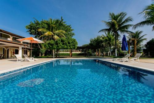 a swimming pool with two chairs and an umbrella and palm trees at Pousada Porto do Rio in Caraguatatuba