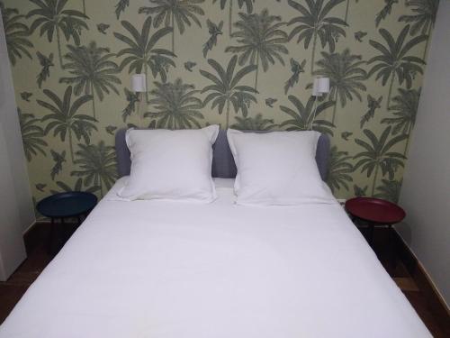 a bed with two pillows in a room with palm wallpaper at Appartement rénové 2 chambres centre historique in Bordeaux