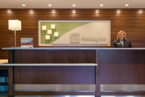 a woman standing behind a counter in a lobby at Holiday Inn Bangor by IHG in Bangor