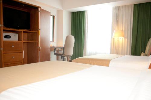 a hotel room with two beds and a chair and a window at Holiday Inn Irapuato by IHG in Irapuato