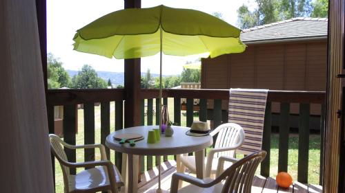 - une table et des chaises sur une terrasse couverte avec un parasol dans l'établissement VVF Cantal Salers Vendes, à Bassignac