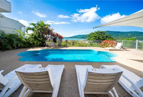 a swimming pool with chairs and a table and an umbrella at OCEAN VIEWS 10 in Airlie Beach