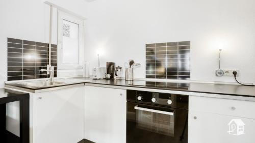 eine Küche mit weißen Schränken und einer schwarzen Arbeitsplatte in der Unterkunft Gästewohnung Köln-Longerich in Köln