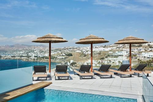 a patio area with chairs, tables and umbrellas at Grand Beach Hotel in Mikonos