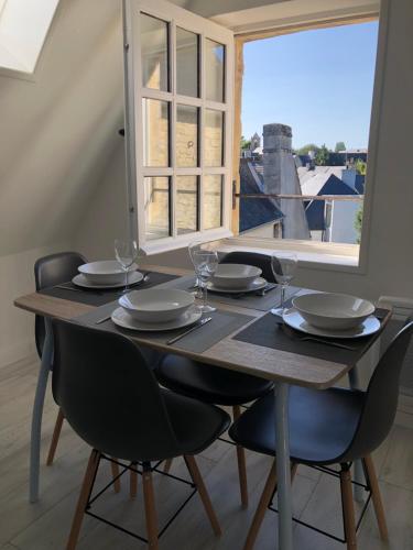 - une table en bois avec des chaises, des assiettes et des verres à vin dans l'établissement Charmant appartement au coeur de Bayeux, à Bayeux
