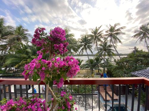 a bunch of pink flowers on a balcony with palm trees at Phuoc Dat Riverside Homestay Hoi An in Hoi An