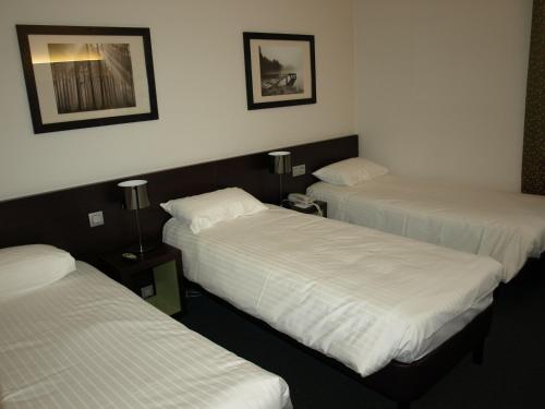 three beds in a room with white sheets at Kyriad Hôtel Orly Aéroport - Athis Mons in Athis-Mons