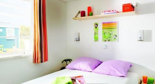 Un dormitorio con una cama con almohadas rosas y una ventana en Camping Les Chèvrefeuilles - Maeva, en Royan
