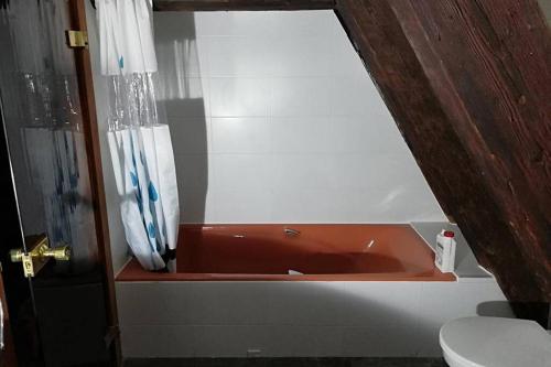 La salle de bains est pourvue d'une baignoire rouge et de toilettes. dans l'établissement La Chaumière, à Strasbourg