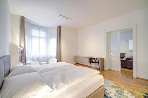 a white bedroom with a large bed and a desk at Bishop Apartments in Brno