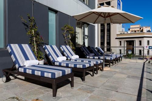 a row of lounge chairs with an umbrella on a patio at Cresta Grande Cape Town in Cape Town