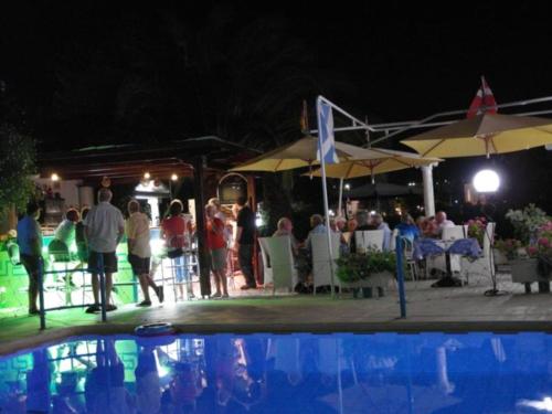 Un groupe de personnes debout autour d'une piscine la nuit dans l'établissement Sun City, à Kato Daratso