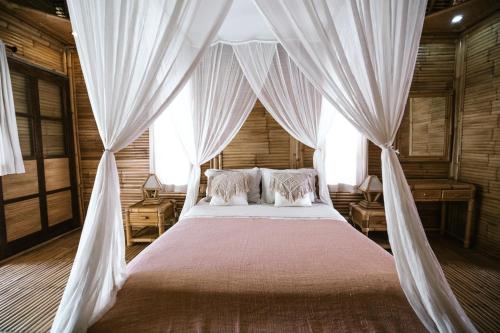 een slaapkamer met een hemelbed en witte gordijnen bij Bamboo Bungalows in Nusa Lembongan