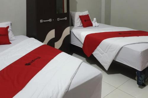 two beds with red and white sheets in a room at RedDoorz @ Hotel Yaki Mamuju in Rimuku