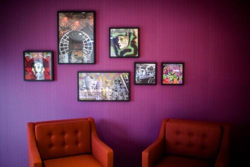 a purple wall with four pictures and two chairs at Holiday Inn Düsseldorf City – Toulouser Allee by IHG in Düsseldorf