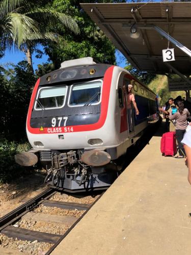a red and white train pulling into a train station at Kandyan Lounge in Kiribatkumbura