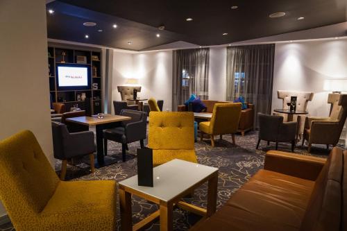 a waiting room with yellow chairs and tables at Holiday Inn Ellesmere Port/Cheshire Oaks by IHG in Ellesmere Port
