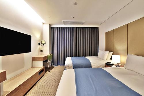 a hotel room with two beds and a flat screen tv at Hotel Whistle Lark in Jeju