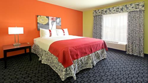 a bedroom with a bed with orange walls and a window at Holiday Inn Garland by IHG in Garland