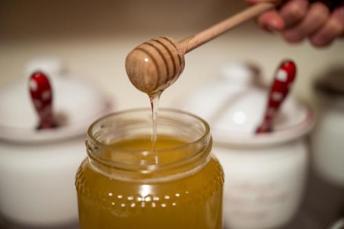 a honey being poured from a wooden spoon into a jar at Meublè Garnì Della Contea in Bormio