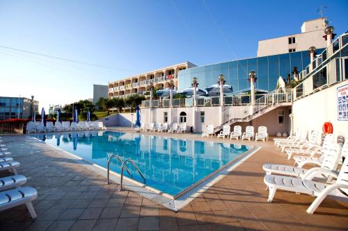 ein Pool mit weißen Stühlen und ein Gebäude in der Unterkunft Hotel Istra Plava Laguna in Poreč