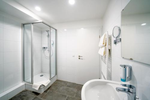 ein weißes Bad mit einer Dusche und einem Waschbecken in der Unterkunft Haus am Zoo Apartments verschiedene Adressen in Düsseldorf